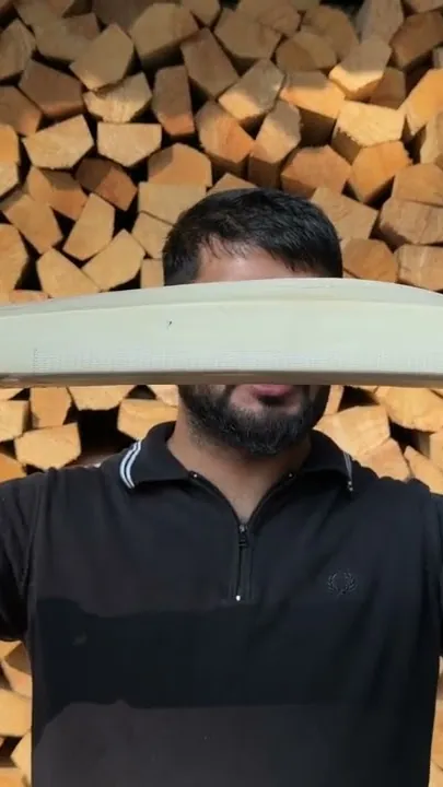 A GSI bat held up in front of stacked willow clefts before it ships to Canada